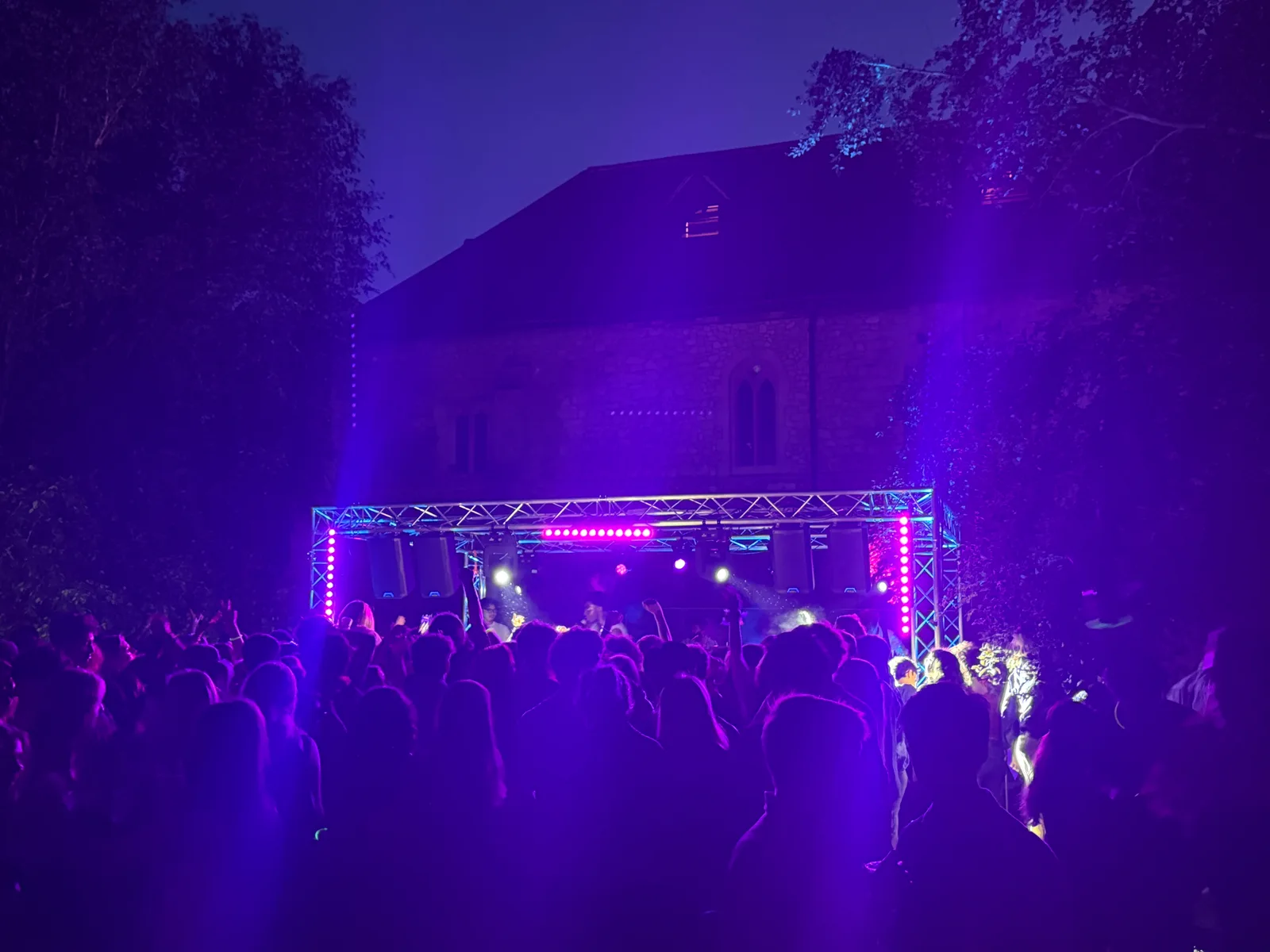 Purple stage lighting over the band and audience on Cambridge University grounds after dark