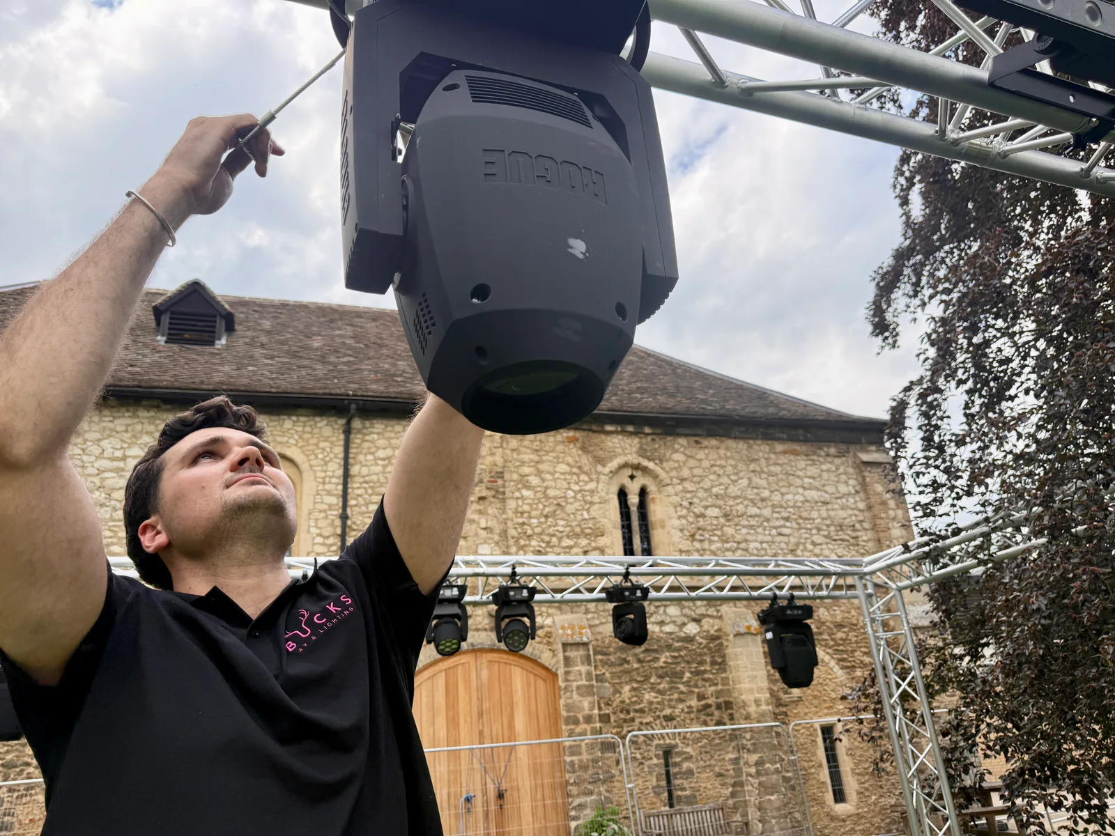 A Bucks AV technician working on a moving-head light attached to the outdoor festival truss
