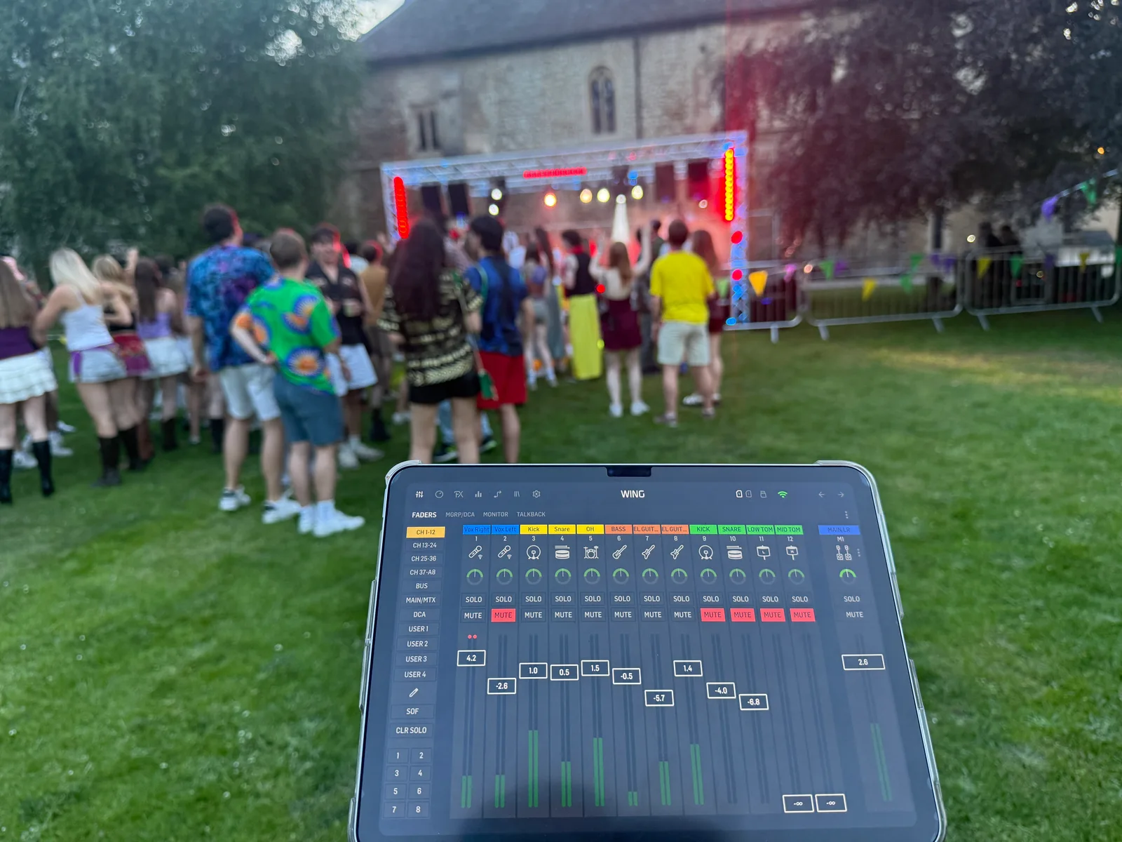 The audio mixing tablet in the foreground with the live stage and festival audience beyond