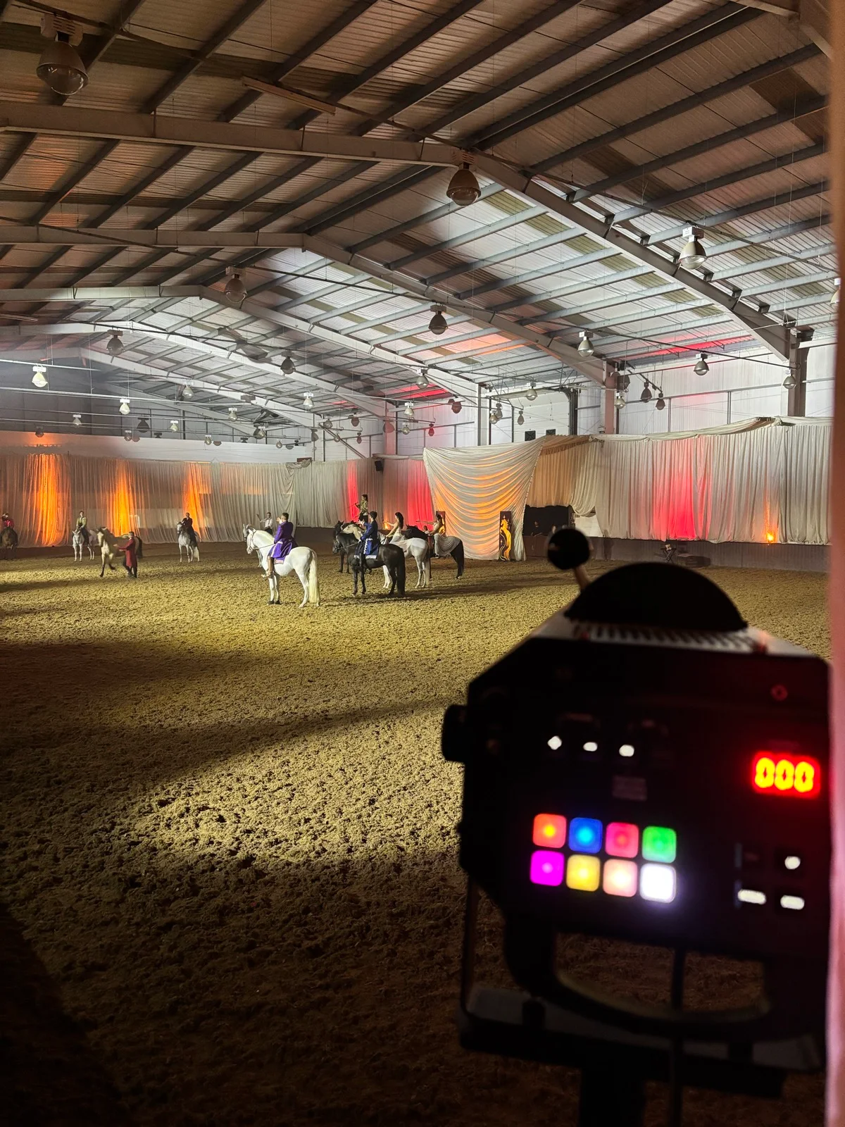Mounted performers in the arena with warm amber and red lighting, seen from a spotlight position